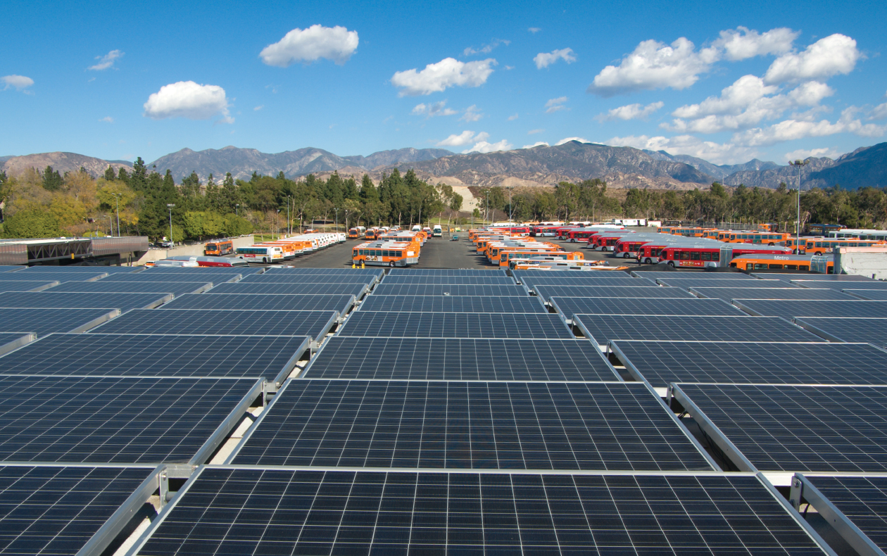 Photo of a solar panel array in front of a parking lot full of Metro buses.
