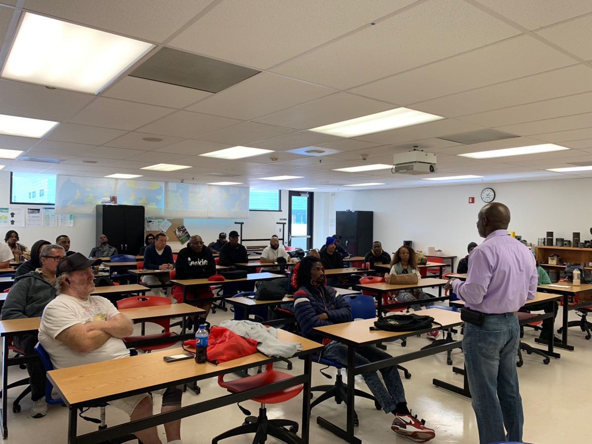 Photo of the side of a man standing in front of a classroom full of students.