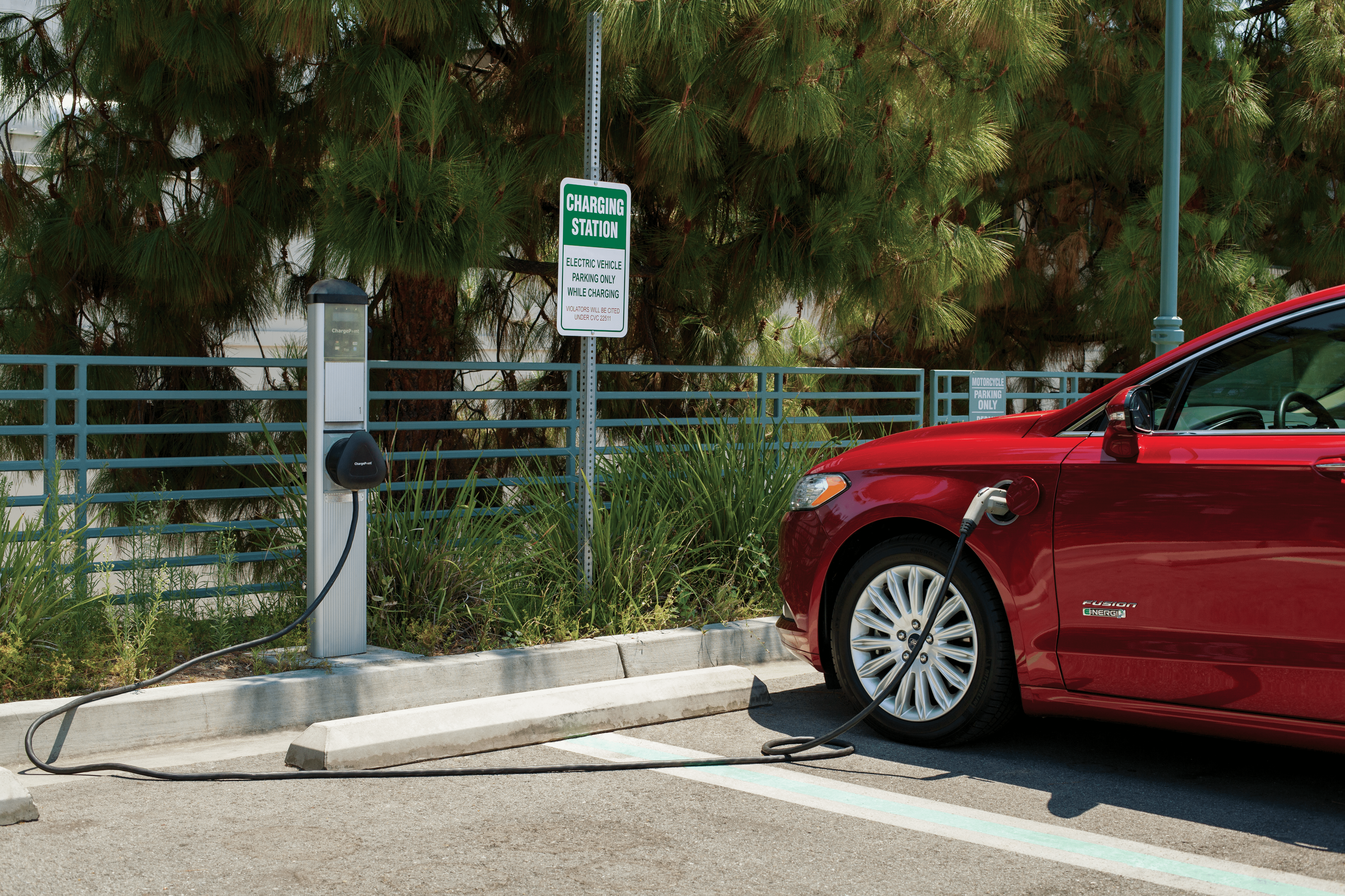 Photo of a red car plugged into an exterior EV charging port in a parking lot. 