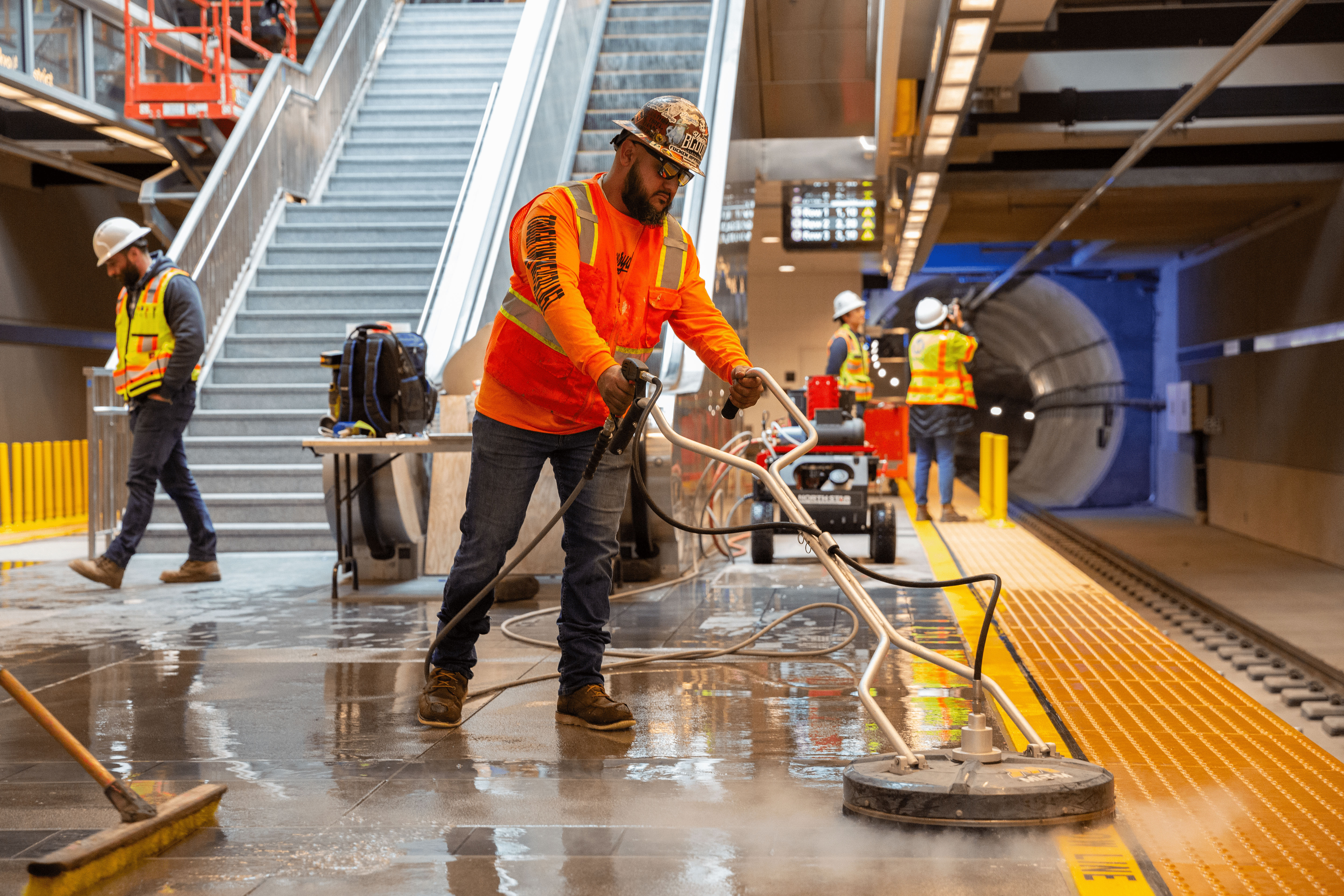Photo of a construction worker in an underground subway station cleaning up water on the platform.